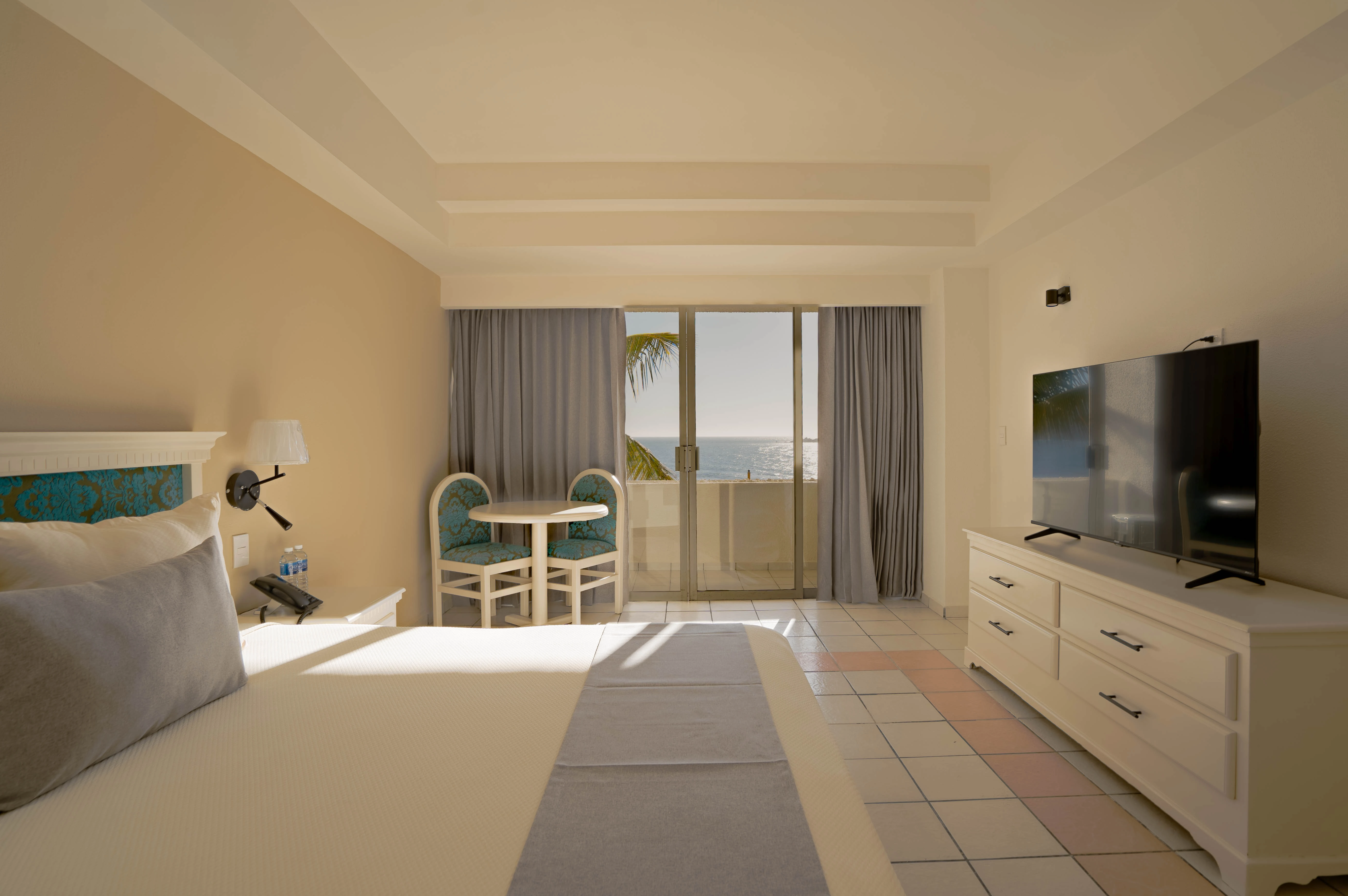 Habitación standard, cama king size, con balcón y vista al mar, mesa con dos sillas del hotel sunset palace Mazatlán